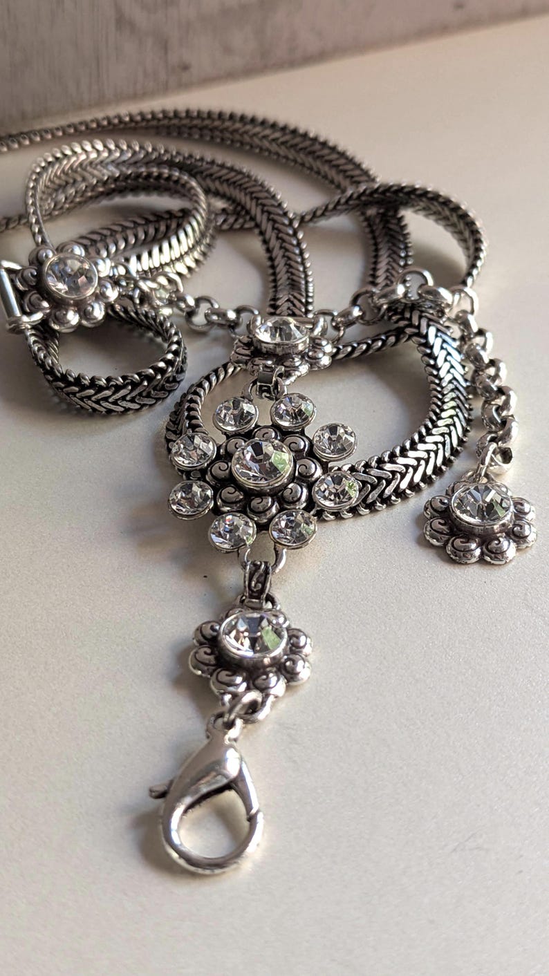 Peut inclure: Collier argent&eacute; avec un pendentif floral et des accents de cristaux transparents. La cha&icirc;ne est tress&eacute;e et se ferme avec un fermoir mousqueton. Le design comprend un anneau et un petit pendentif fleur.