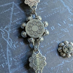 Peut inclure: Collier argent&eacute; avec des motifs de pendentifs floraux et circulaires. Le collier est dot&eacute; d'un fermoir mousqueton et d'une petite boucle d'oreille assortie en forme de fleur avec un centre en cristal transparent. Le bijou est pos&eacute; sur un fond de carte.