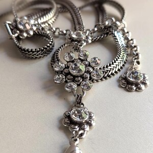 Peut inclure: Un collier argent&eacute; avec un pendentif floral et des cristaux transparents &eacute;tincelants. Le collier pr&eacute;sente une cha&icirc;ne tress&eacute;e et un bracelet assorti avec un fermoir floral. Le pendentif a un motif floral avec plusieurs cristaux.