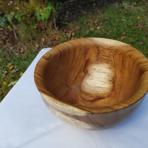 May include: A handcrafted wooden bowl with a natural, warm brown finish. The bowl has a smooth, rounded shape and visible wood grain patterns. This decorative bowl is suitable for serving or display.
