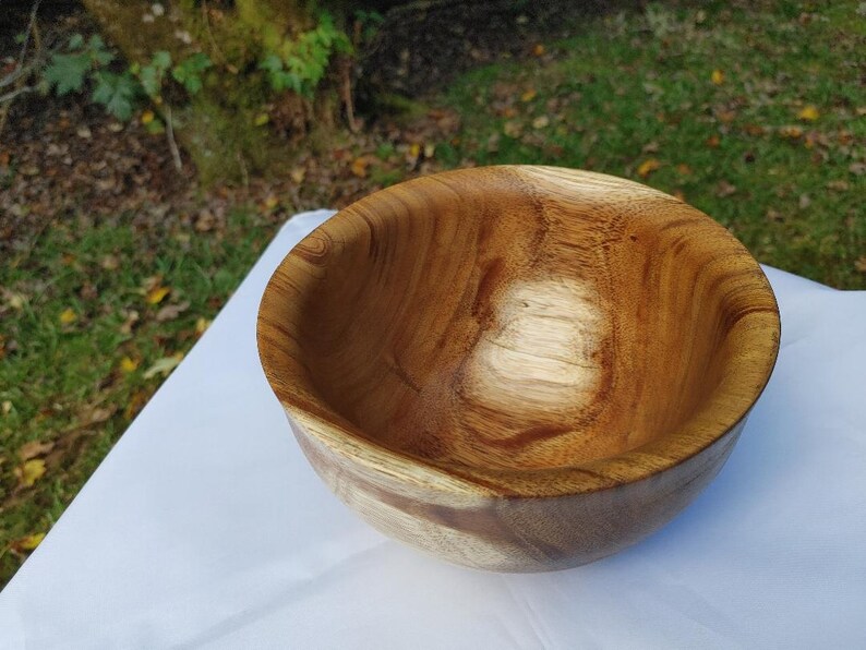 May include: A handcrafted wooden bowl with a natural, warm brown finish. The bowl has a smooth, rounded shape and visible wood grain patterns. This decorative bowl is suitable for serving or display.