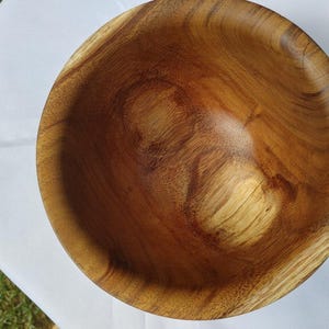May include: A handcrafted wooden bowl with a natural wood grain pattern. The bowl is round with a smooth, polished interior and a warm, brown color. The bowl is likely used for serving food or as a decorative item.