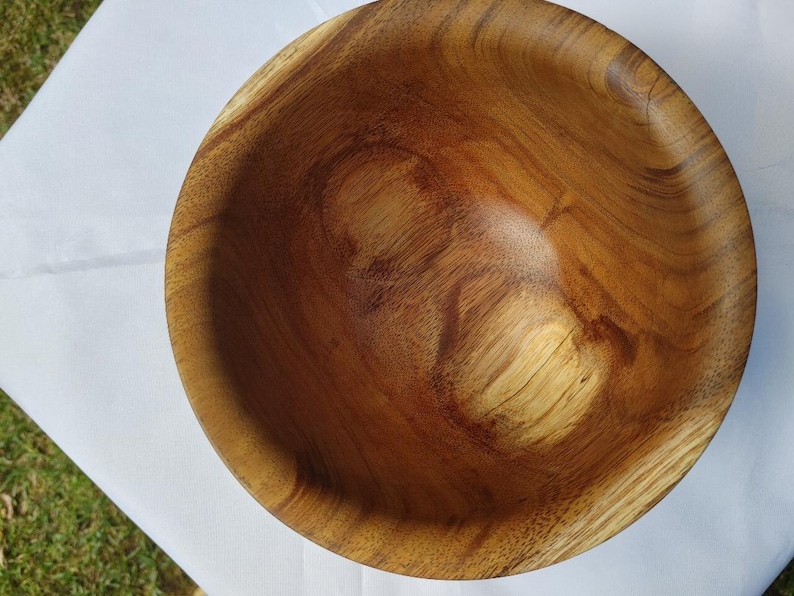 May include: A handcrafted wooden bowl with a natural wood grain pattern. The bowl is round with a smooth, polished interior and a warm, brown color. The bowl is likely used for serving food or as a decorative item.