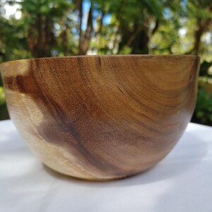 May include: A handcrafted wooden bowl with a natural, warm brown color. The bowl has a smooth, curved design and a visible wood grain pattern. The bowl is likely made from a hardwood and is suitable for serving food or as a decorative item.