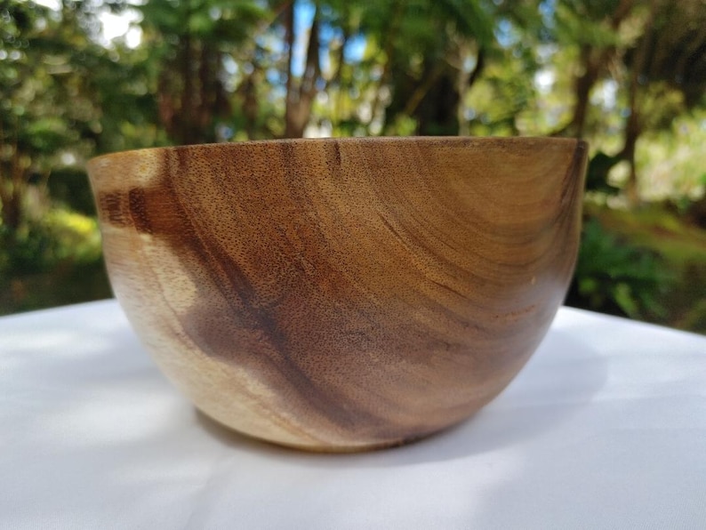 May include: A handcrafted wooden bowl with a natural, warm brown color. The bowl has a smooth, curved design and a visible wood grain pattern. The bowl is likely made from a hardwood and is suitable for serving food or as a decorative item.