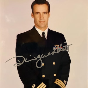 Puede incluir: Retrato de un hombre con uniforme naval azul marino con botones dorados y rayas en las mangas. El uniforme incluye una camisa blanca con cuello y una corbata negra. La imagen está firmada con tinta plateada.
