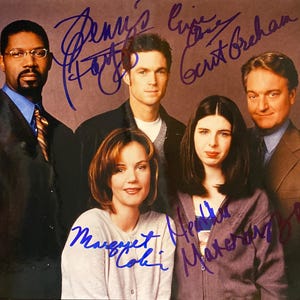 May include: A group photo of five people, likely actors, with signatures in blue ink. The people are dressed in various outfits, including suits, sweaters, and casual wear. The photo has a vintage feel.