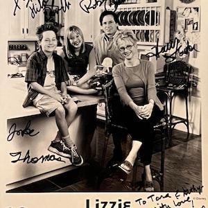 Op de afbeelding: Zwart-witfoto van de cast van de Disney Channel-show "Lizzie McGuire". De castleden hebben handtekeningen. Het logo van de show en het Disney Channel-logo staan onderaan.