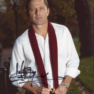 May include: A white long-sleeved shirt with subtle textured embroidery on the chest, paired with a long, solid dark red scarf. The shirt features a button-down collar and is worn with dark trousers. A silver-toned wristwatch is visible on the wrist.