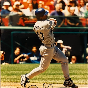 Peut inclure: Un joueur de baseball en uniforme gris avec le nom "Mondesi" et le numéro 13 dans le dos frappe la balle. Le joueur porte un casque bleu et des crampons noirs et gris. L'image est signée à l'encre noire.
