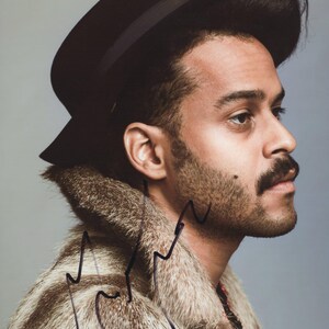 May include: A side profile portrait of a person wearing a black hat and a fur coat with brown and cream tones. The person has a mustache and a beard. The image has a neutral background.