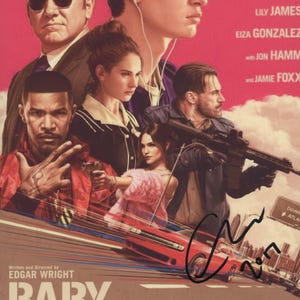 May include: A movie poster for Baby Driver featuring a cast of characters in front of a red car on a pink background. The poster includes the text Baby Driver, Edgar Wright, and actor names, with a black ink signature across the lower right side.