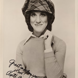 May include: Black and white photograph of a person wearing a plaid hat, light-colored sweater, and collared shirt. The photo includes a handwritten signature that reads "Great meeting you! Love! Ruth Buzzi 86."