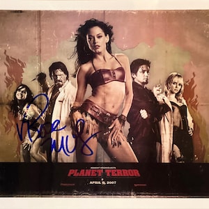 May include: A promotional poster for the film "Planet Terror" featuring a group of actors. The poster has a distressed, vintage aesthetic with the film's title and release date at the bottom. The actors are posing in front of a distressed wall.
