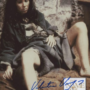 May include: A vintage photograph featuring a woman in a period costume, seated against a stone wall. She wears a dark, draped garment. The image includes an autograph and the title "The Name of the Rose."