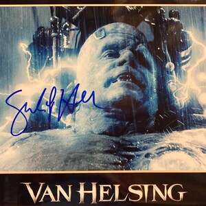 May include: A framed image from the movie "Van Helsing" featuring a character with a pale complexion, surrounded by electrical effects. The image is signed in blue ink. The movie title is displayed at the bottom.