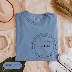 May include: A blue jean colored t-shirt with a round graphic that says "When you pass through the waters, I will be with you." The graphic includes the state of Texas and the Bible verse Isaiah 43:2.