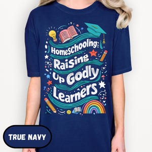 May include: A navy blue t-shirt with the text "Homeschooling: Raising Up Godly Learners" in a colorful design. The design includes a rainbow, pencils, a graduation cap, and an open book.
