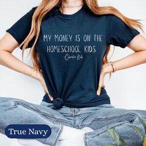 May include: A navy blue t-shirt with the text "MY MONEY IS ON THE HOMESCHOOL KIDS - Charlie Kirk" in white. The shirt is a crew neck and is being worn.