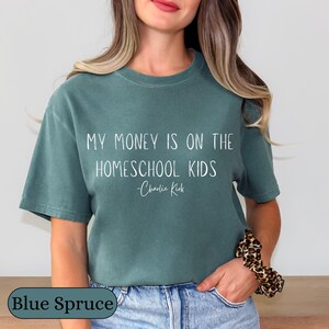 May include: Blue spruce-colored t-shirt with the text "MY MONEY IS ON THE HOMESCHOOL KIDS - Charlie Kirk" in white. The shirt is a crew neck style and is made of a soft material.