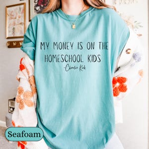 May include: Seafoam green t-shirt with the text "MY MONEY IS ON THE HOMESCHOOL KIDS - Charlie Kirk" in black. The shirt is a solid color and has short sleeves. The shirt is part of a clothing collection.