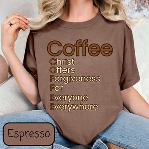 Puede incluir: Una camiseta marrón con el texto "Coffee" en letras marrones grandes. Las letras de "Coffee" están delineadas en un color marrón más claro. Debajo de la palabra "Coffee", las letras "C.O.F.F.E.E." están deletreadas verticalmente, con cada letra representando una palabra: Christ Offers Forgiveness For Everyone Everywhere.