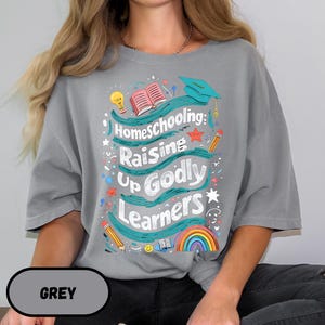 May include: A gray t-shirt with the words "Homeschooling: Raising Up Godly Learners" in a colorful design. The design includes a rainbow, pencils, a graduation cap, and an open book.