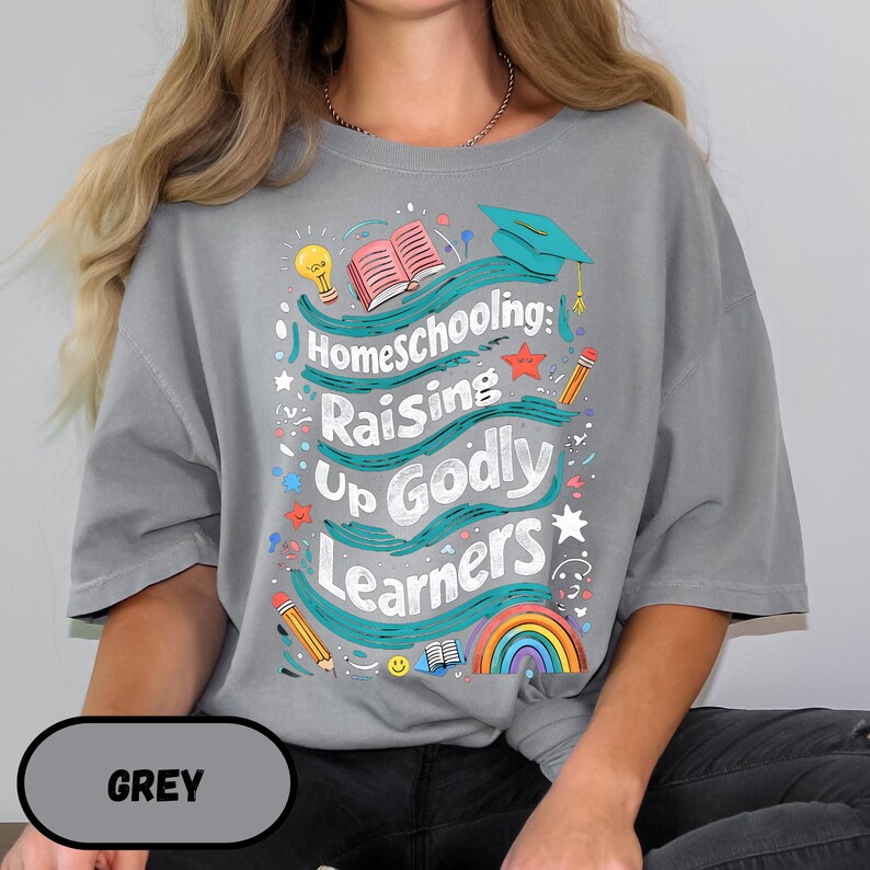 May include: A gray t-shirt with the words "Homeschooling: Raising Up Godly Learners" in a colorful design. The design includes a rainbow, pencils, a graduation cap, and an open book.