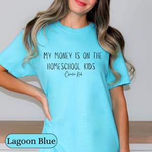 May include: Lagoon blue t-shirt with the text "MY MONEY IS ON THE HOMESCHOOL KIDS - Charlie Kirk" in black. The shirt is a solid color and has a round neckline.