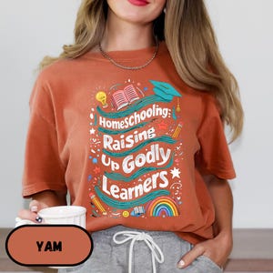 May include: Rust-colored t-shirt with the text "Homeschooling: Raising Up Godly Learners" in a colorful design. The design includes a graduation cap, pencils, a rainbow, and an open book. The shirt is a comfortable, casual style.