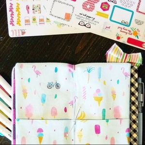 May include: A white notebook with a zipper closure and a colorful pattern of pink flamingos, ice cream cones, popsicles, palm trees, and bicycles. The notebook is open to reveal a blank page and a second page with the same pattern. The notebook is tied together with a white string.