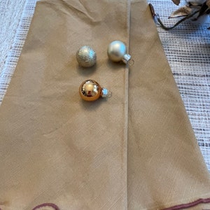 May include: A tan tree skirt with a scalloped edge and three gold and silver ornaments.