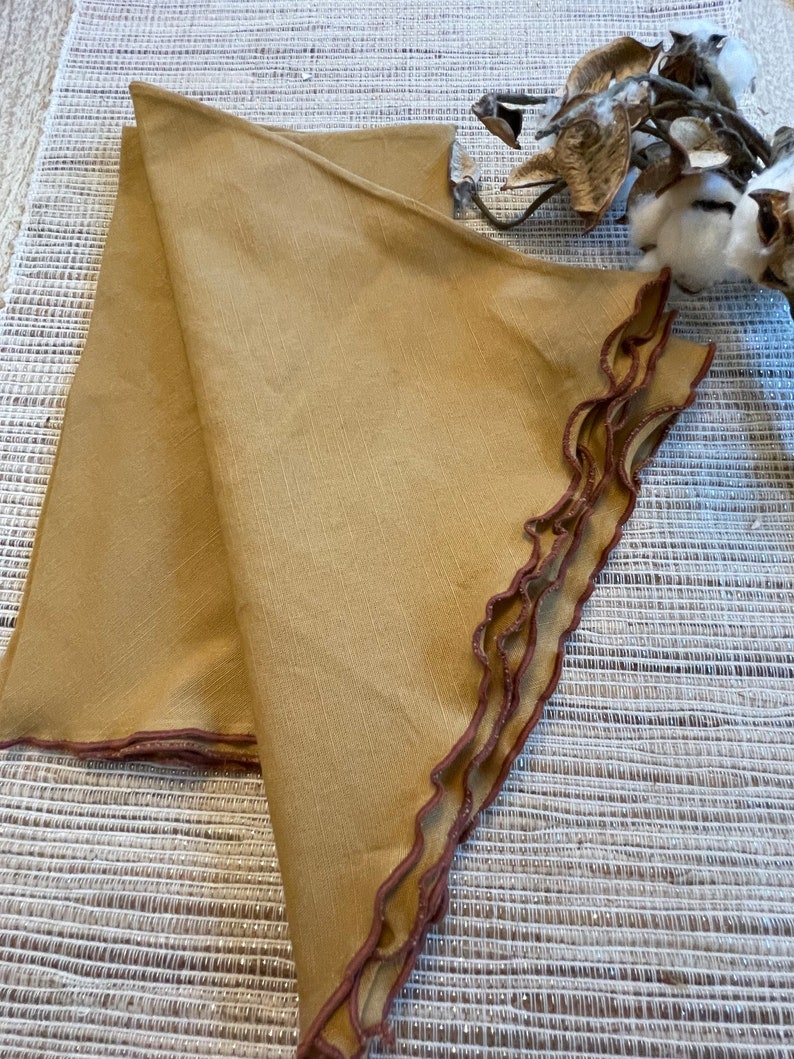 May include: Two folded brown linen napkins with a scalloped edge and a brown trim.