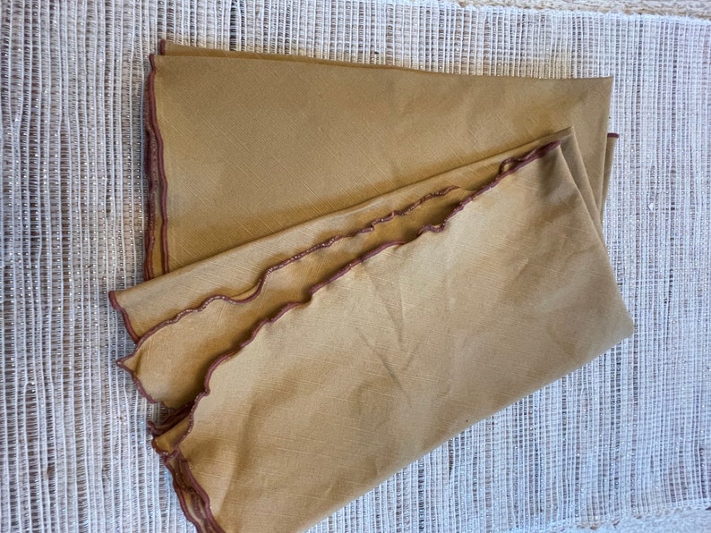 May include: Two brown linen napkins with scalloped edges and a brown embroidered trim.