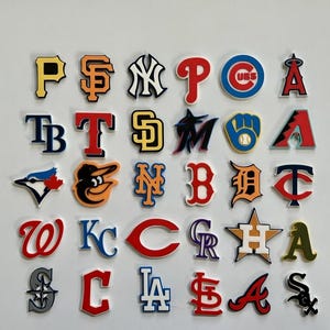 Puede incluir: Una colección de logotipos coloridos de equipos de la MLB, incluidos los Yankees, los Dodgers y los Cubs. Cada logotipo tiene una combinación única de forma y color, como el logotipo naranja de los Giants y el logotipo rojo de los Cardinals. Los logotipos están dispuestos sobre un fondo blanco.