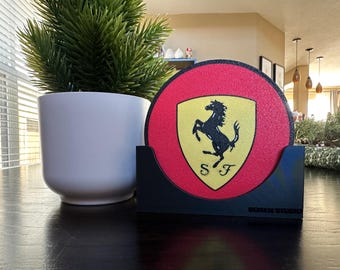 May include: A black and yellow Ferrari logo on a red round coaster. The coaster is in a black holder with the words "Modern Studio" printed on the bottom.
