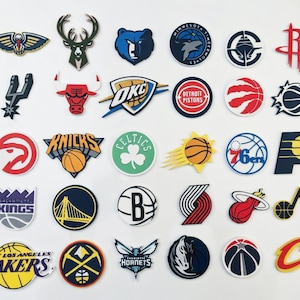 May include: A collection of colorful NBA team logo patches, including the Lakers, Celtics, and Bulls. The patches feature various shapes and designs, with vibrant colors and detailed graphics. These patches are likely for apparel or accessories.