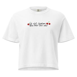 May include: A white short-sleeve t-shirt featuring the black text "Oh shit, Graham. You know this one?" centered on the chest. The text is flanked by two small red cherry illustrations with green stems, one on each side of the phrase.