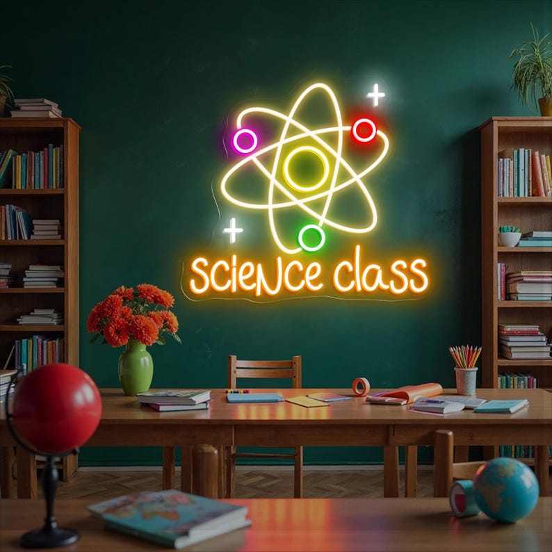May include: A neon sign in a classroom setting displays a colorful atom symbol with the words "science class" in orange. The sign is mounted on a dark green wall. Bookshelves, a table, and a globe are visible.