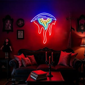 May include: A neon eye-shaped sign with blue, yellow, and red lights is displayed on a red wall. Below, a black sofa is adorned with red cushions. A black table with books and candles sits in front of the sofa. The room has a gothic theme.