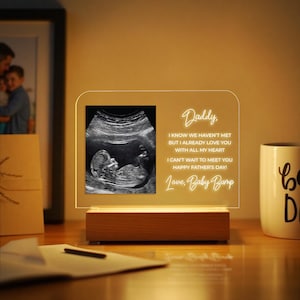 May include: A lighted acrylic plaque featuring a sonogram image and the text "Daddy, I know we haven't met but I already love you with all my heart. I can't wait to meet you Happy Father's Day! Love, Baby Bump." The plaque has a wooden base.
