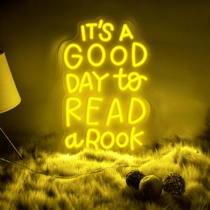 May include: Yellow neon sign with the text "It's a good day to read a book".