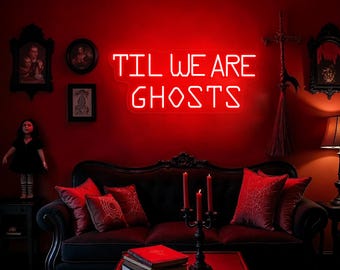 Op de afbeelding: Een rood neonbord met de tekst "Til We Are Ghosts" op een rode muur. Voor het bord staat een zwarte bank met rode kussens. Er staan kaarsen en boeken op een salontafel voor de bank.