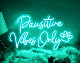May include: A teal neon sign with the text "Positive Vibes Only" and a paw print. The sign is on a fuzzy teal surface.
