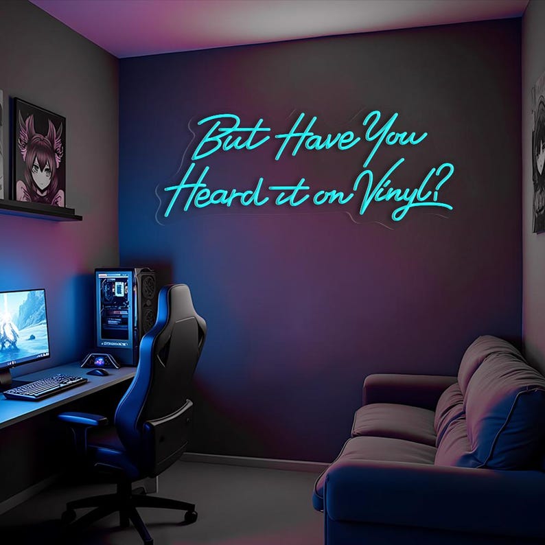 May include: A blue neon sign with the text "But Have You Heard it on Vinyl?" hanging on a dark grey wall in a room with a sofa, a desk, and a gaming chair.
