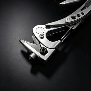 以下が含まれることがあります： ガラスブレーカーの先端、カラビナクリップ、一体型プライヤーを備えたシルバーカラーのマルチツール。金属製のツールはブラッシュ仕上げで、ハンドルに沿ってネジと切り抜きディテールが見え、暗い背景に配置されています。