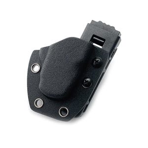 Könnte beinhalten: Eine schwarze, texturierte Kydex-Scheide mit einer geformten Aussparung für ein Werkzeug, befestigt mit zwei schwarzen Kreuzschlitzschrauben und drei silberfarbenen Metallösen am Rand, verbunden mit einem schwarzen Kunststoff-Gürtelclip mit gezacktem Rand.