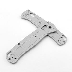Peut inclure: Deux plaquettes de manche de couteau en métal gris clair avec un motif texturé en forme de grille. Chaque pièce présente des trous circulaires pré-percés pour l'assemblage, un profil incurvé et une découpe rectangulaire près du sommet.