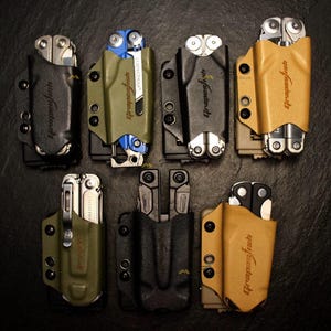 Op de afbeelding: Zeven multitool-foedralen in diverse kleuren zoals zwart, olijfgroen en beige, elk met de merknaam Grapefish in reliëf op de voorzijde. Deze gevormde houders zijn ontworpen om opvouwbare multitools stevig vast te houden met metalen klinknagels.