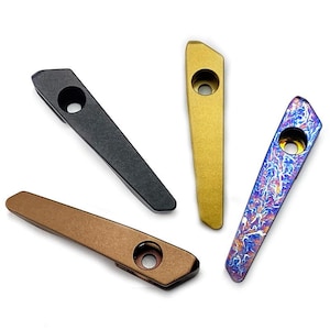 Puede incluir: Cuatro pipas de metal alargadas y cónicas con una única abertura circular cerca de la parte superior. El conjunto incluye una negra mate, una dorada metálica, una de tono bronce y una iridiscente con un patrón azul, morado y naranja.